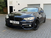 Load image into Gallery viewer, A dark metallic blue BMW M4 coupe parked on a paved driveway in front of a white building with garage doors.
