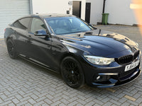 Load image into Gallery viewer, A dark metallic blue BMW 4 Series Gran Coupe parked on a gray paved driveway in front of a white building.
