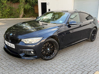 Load image into Gallery viewer, A dark metallic gray BMW 4 Series coupe sedan parked on a gray paved driveway in front of a garage door and house building.
