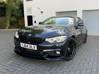 Load image into Gallery viewer, A dark metallic blue BMW 4 Series coupe parked on a gray paved driveway in front of a white building with garage doors.
