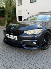 Load image into Gallery viewer, A dark metallic blue BMW F32 coupe parked on a gray paved driveway in front of a white building. The car is shown from a low front-three-quarter angle, highlighting the front grille, headlights, front bumper, and black multi-spoke wheels.
