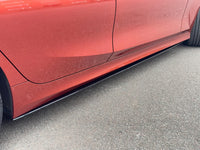 Load image into Gallery viewer, A close-up side view of a red car showing a black side skirt or underbody trim installed along the lower side panel, positioned above gray asphalt pavement.
